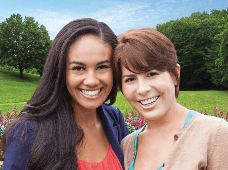 Two young women leaning into each other smiling