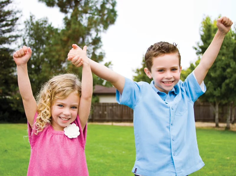 Young girl and boy holding their hands in the air and smiling
